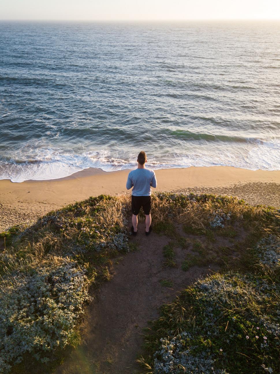 Free Image of Person kneeling on shore overlooking beach 