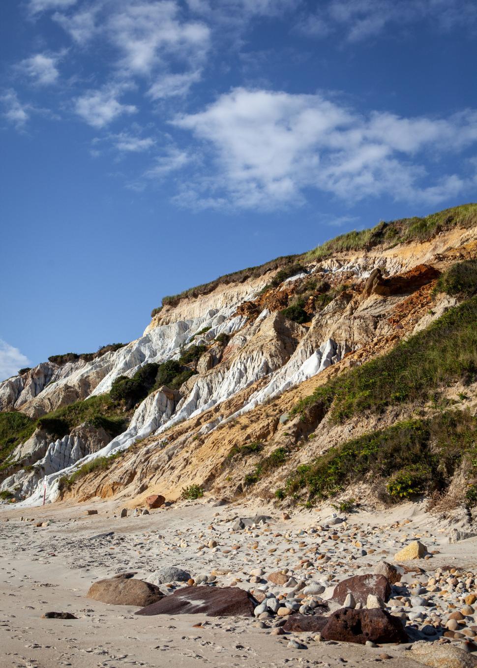 Free Image of Cliff face over a pebbled beach under blue sky 