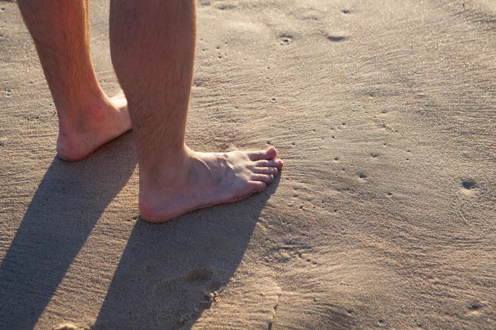 Free Image of Human feet standing on sandy beach at sunset 