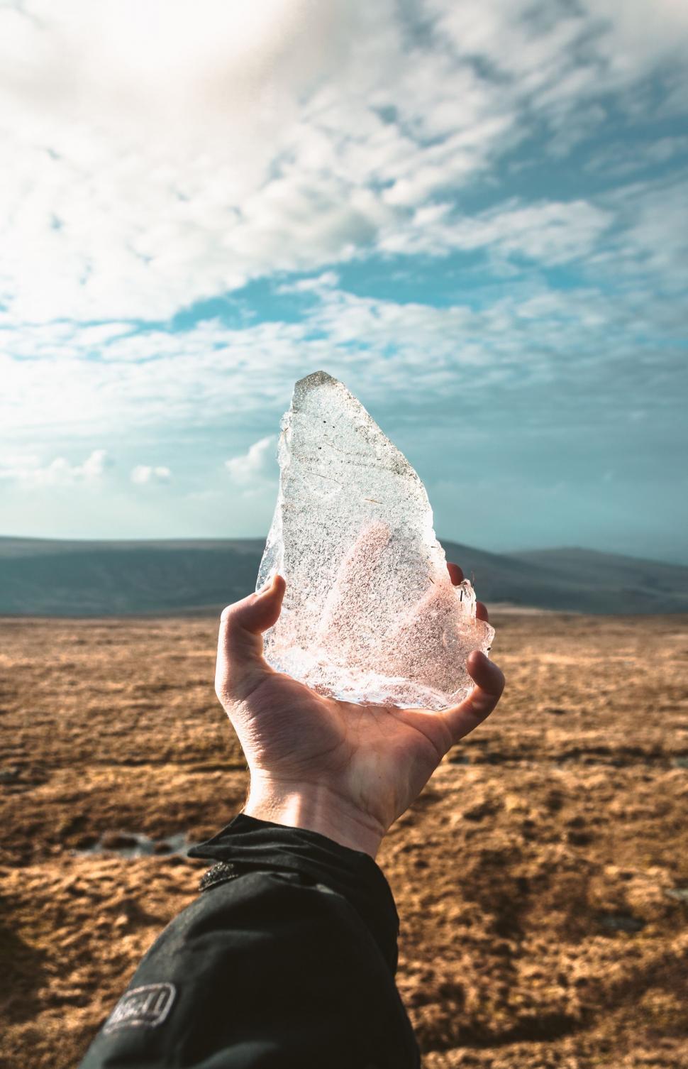 Free Image of Hand holding a clear ice shard against barren landscape 
