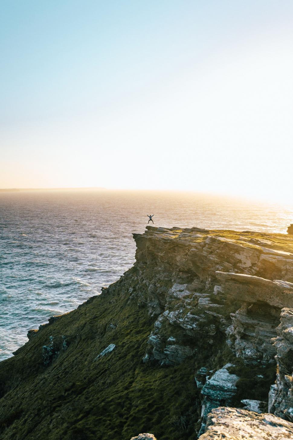 Free Image of Person on cliff edge with outstretched arms at sunset 