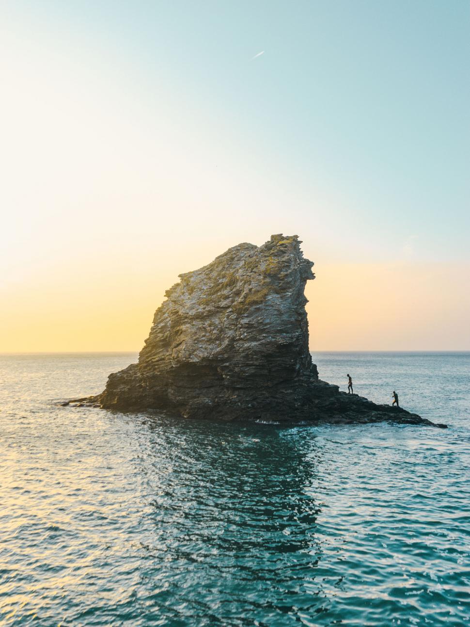 Free Image of Rocky sea stack with people for scale at golden hour 