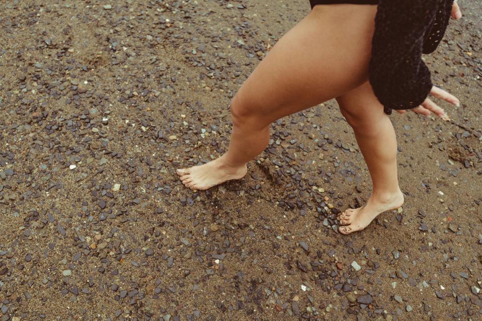 Free Image of Woman walking barefoot on pebble beach 