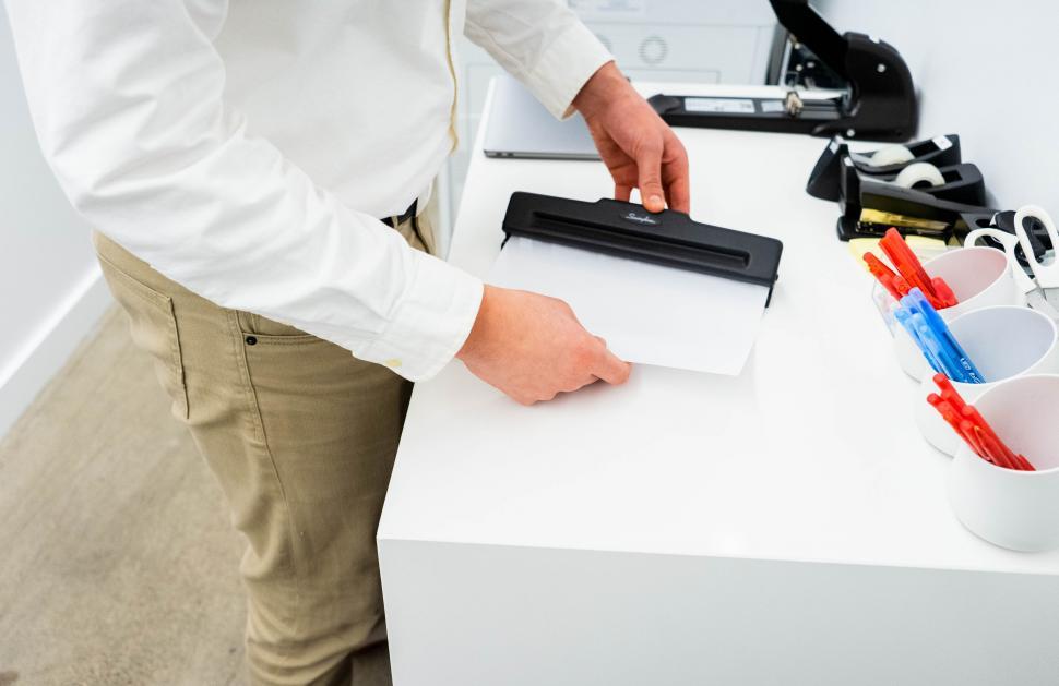 Free Image of Man using a paper binder on a desk 