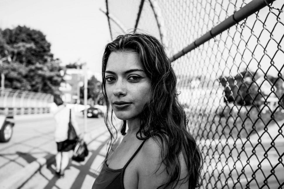 Free Image of Black and white portrait by a chain fence 