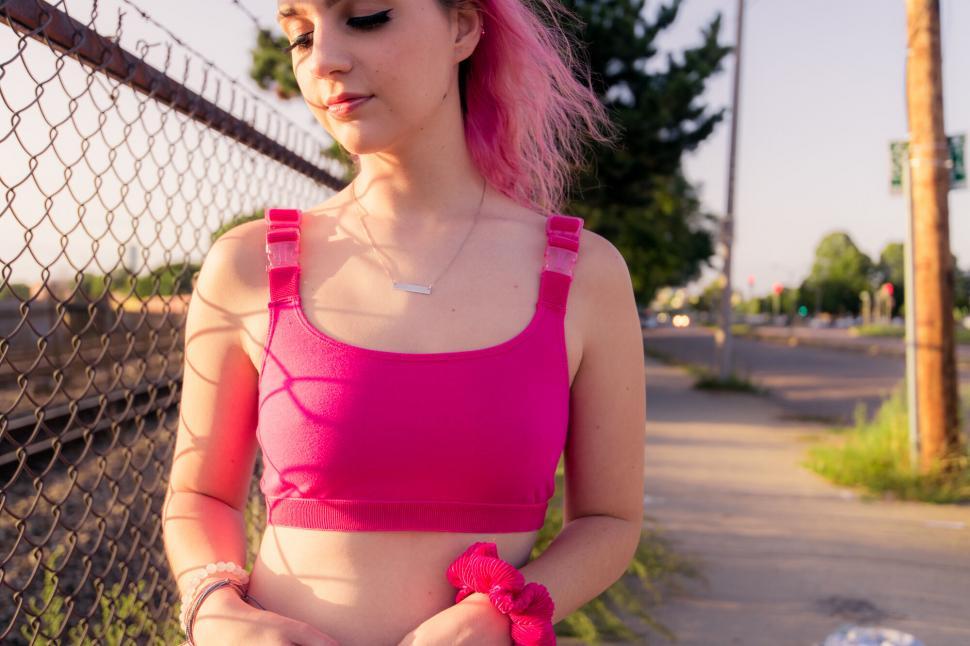 Free Image of Woman in pink sports bra by urban fence 