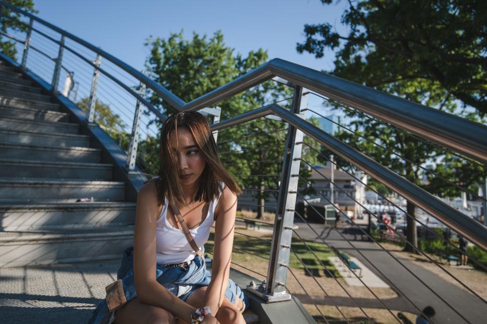 Free Image of Young woman sitting on stair rail in the sun 