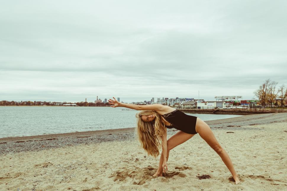 Free Image of Woman stretching on beach with city view 