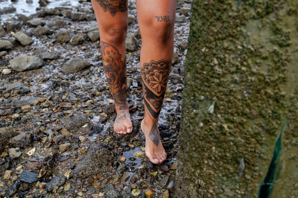 Free Image of Detailed leg tattoo on beach with pebbles and shells 