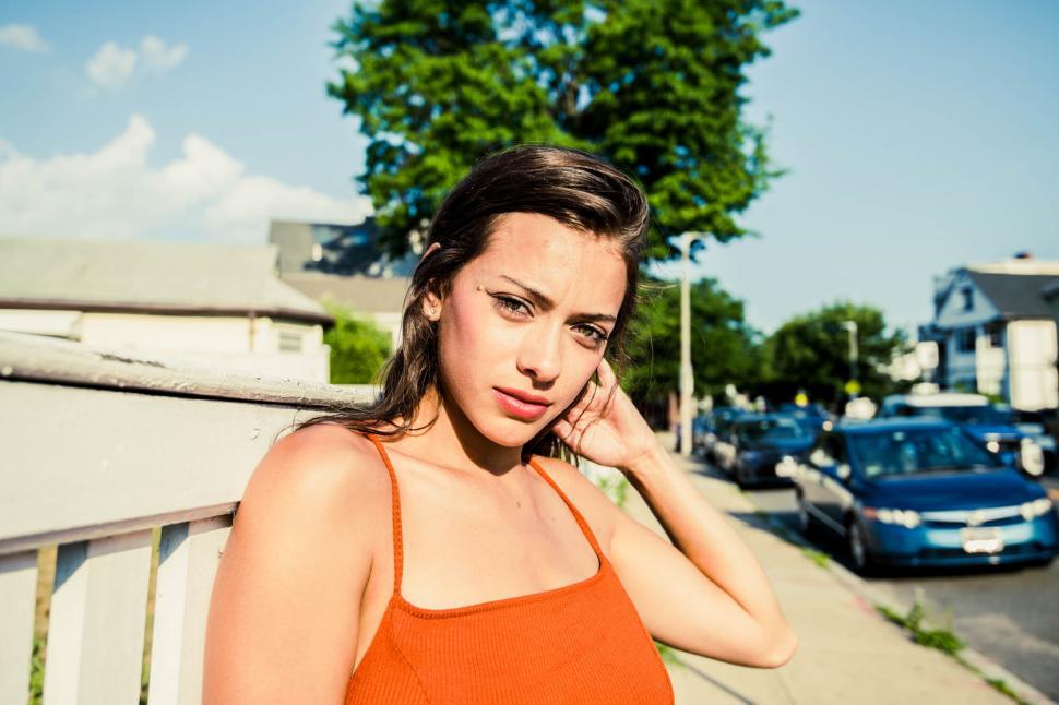 Free Image of Squinting woman in orange top holding hair 