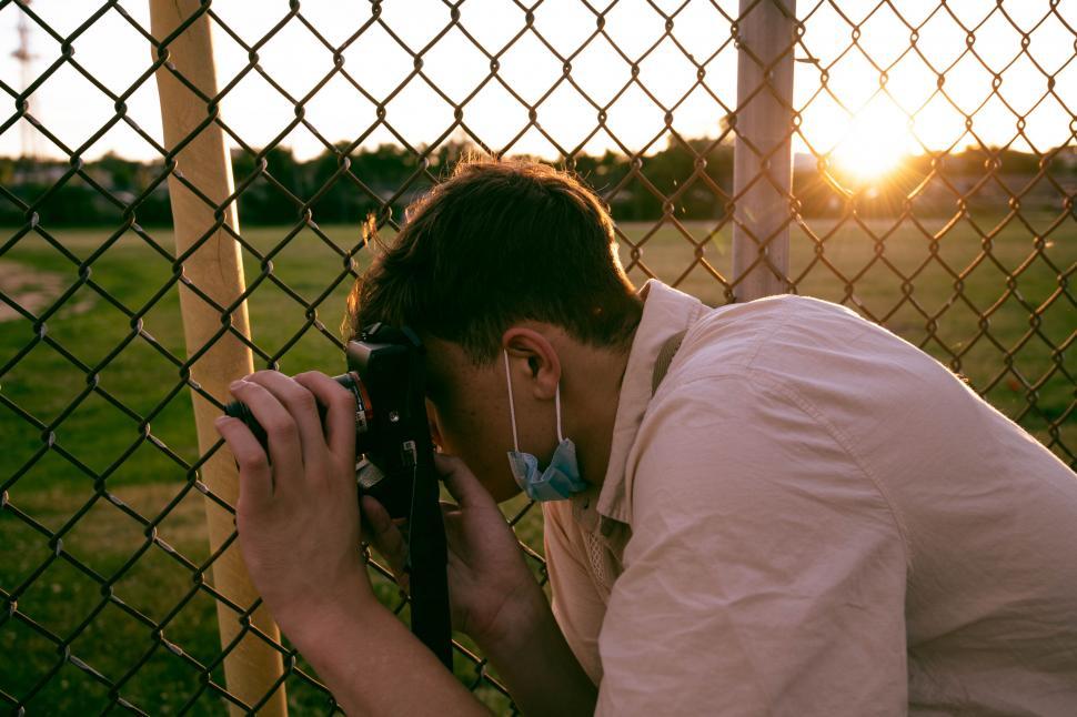 Free Image of Young male photographer behind chain fence 