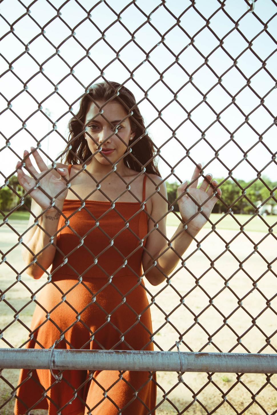 Free Image of Woman Peering Through Chain-link Fence 