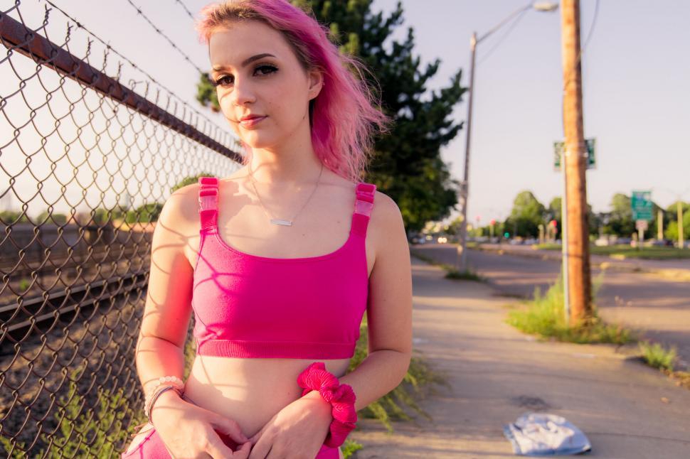 Free Image of Pink-haired woman in sporty outfit by fence 