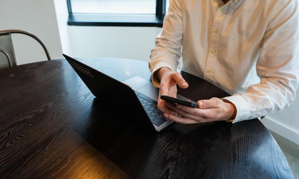 Free Image of Man using smartphone and laptop at desk 