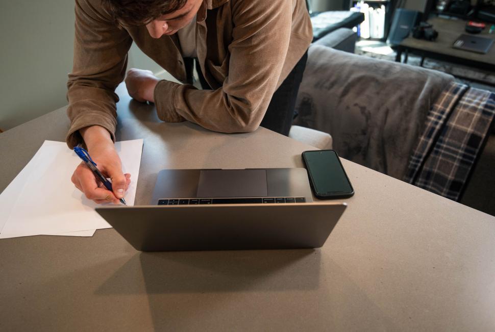 Free Image of Man writing on paper beside electronics 