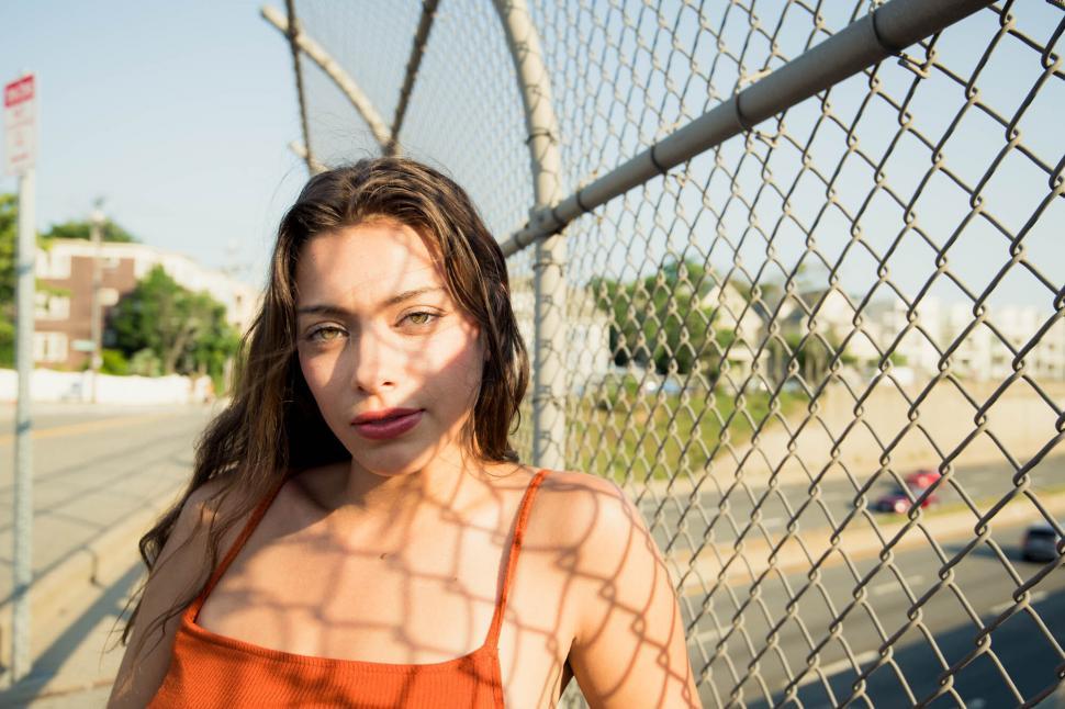 Free Image of Woman leaning on chain-link fence in sunlight 