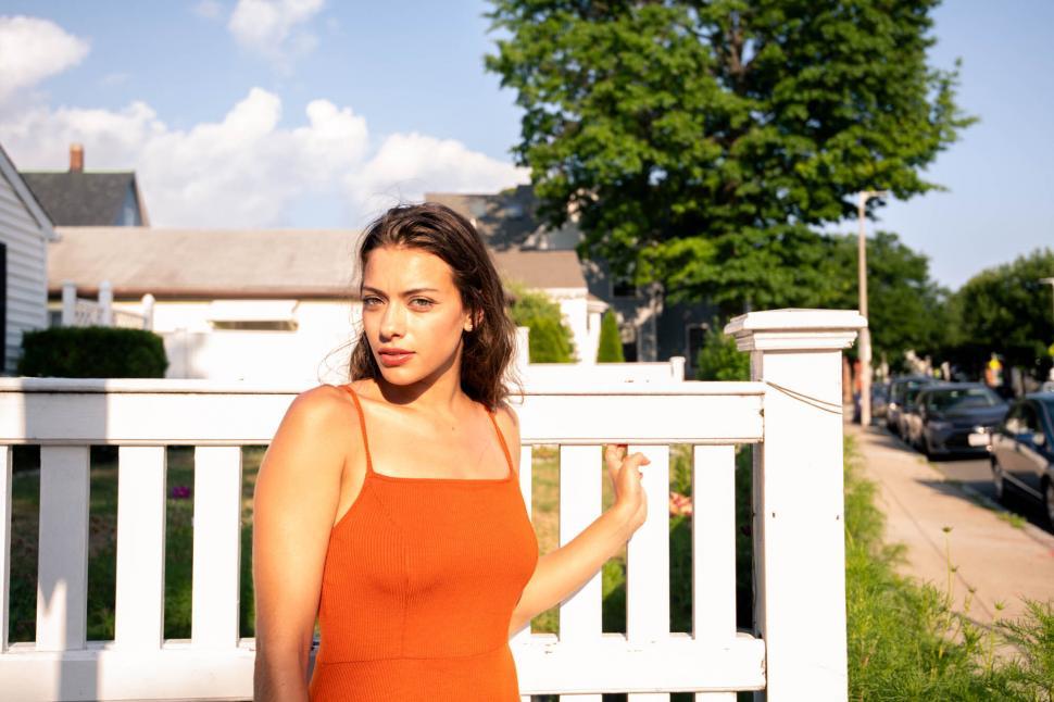 Free Image of Young woman by white fence in sunlight 
