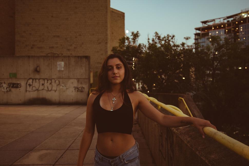 Free Image of Urban woman in tank top by yellow railing 