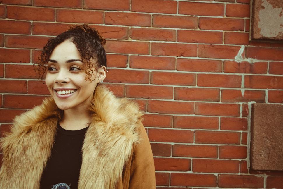 Free Image of Smiling woman in fur coat by brick wall 