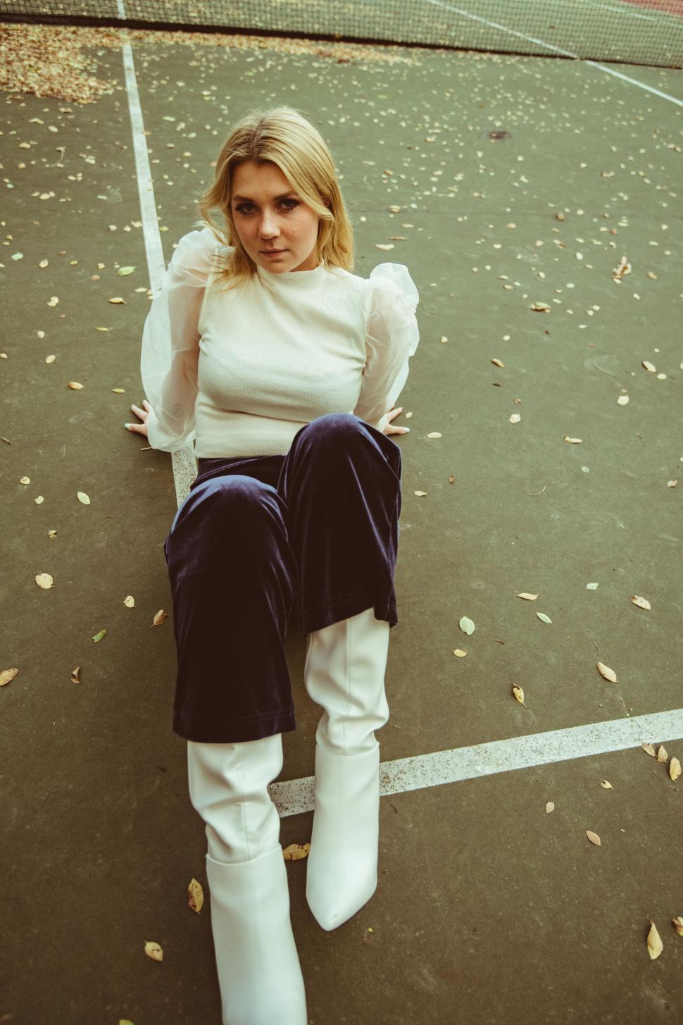 Free Image of Elegant blonde seated on tennis court 