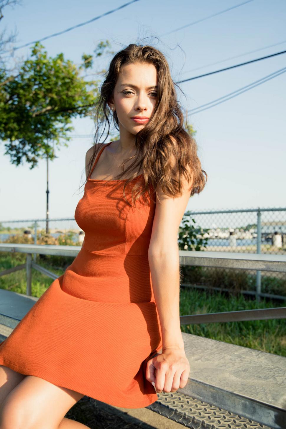 Free Image of Woman in orange dress sitting on bench 