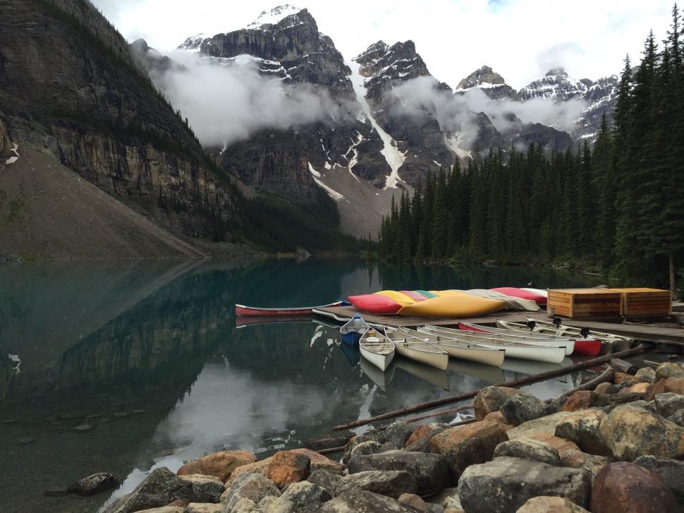 Free Image of Canoes on a calm lake with mountain backdrop 