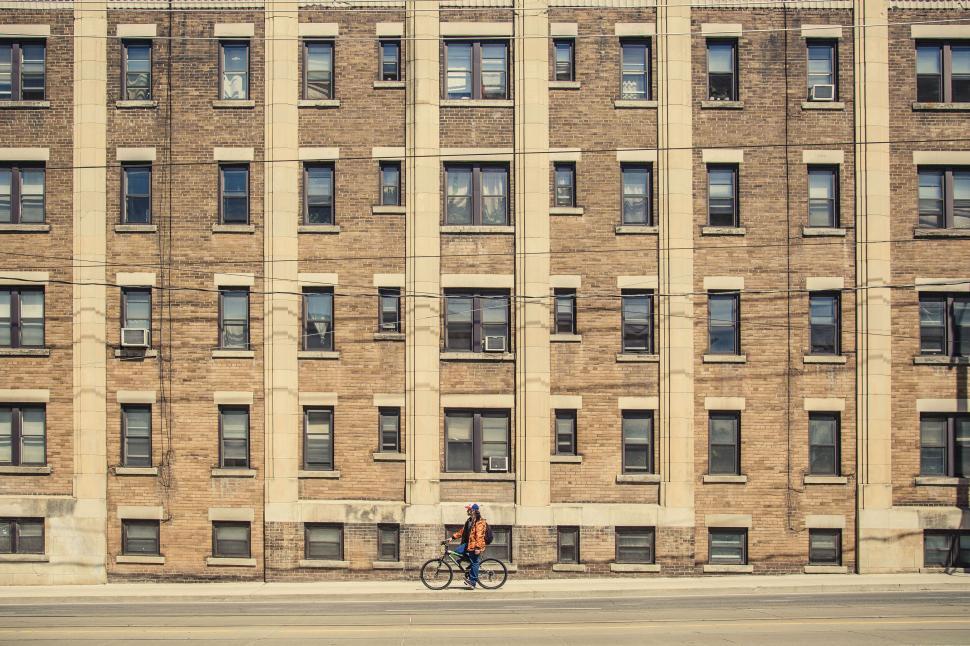 Free Image of Cyclist passing by a large brick building 