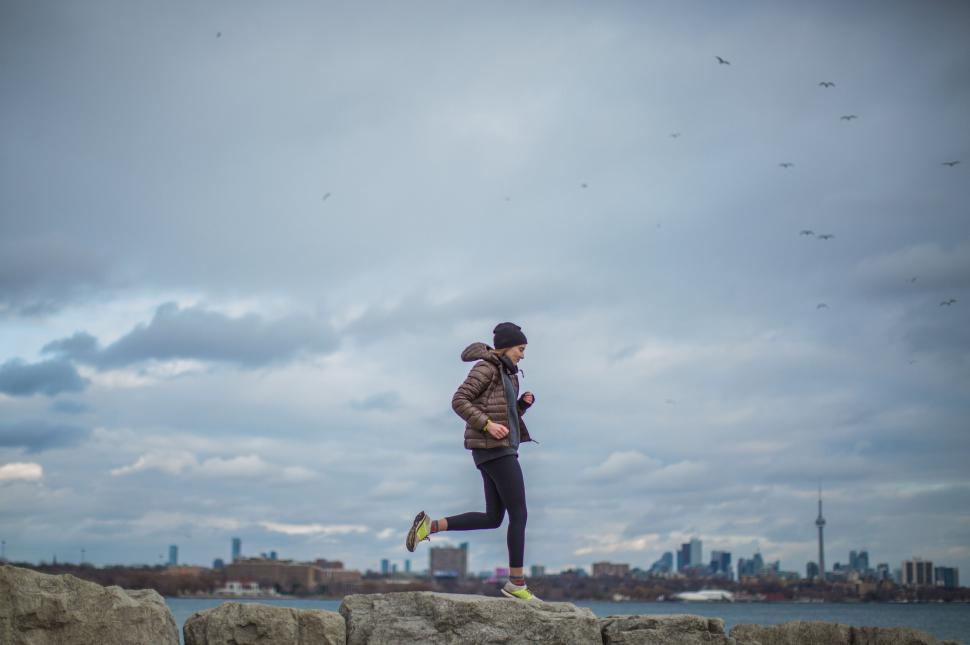 Free Image of Woman Jogging by the Seashore with Cityscape 