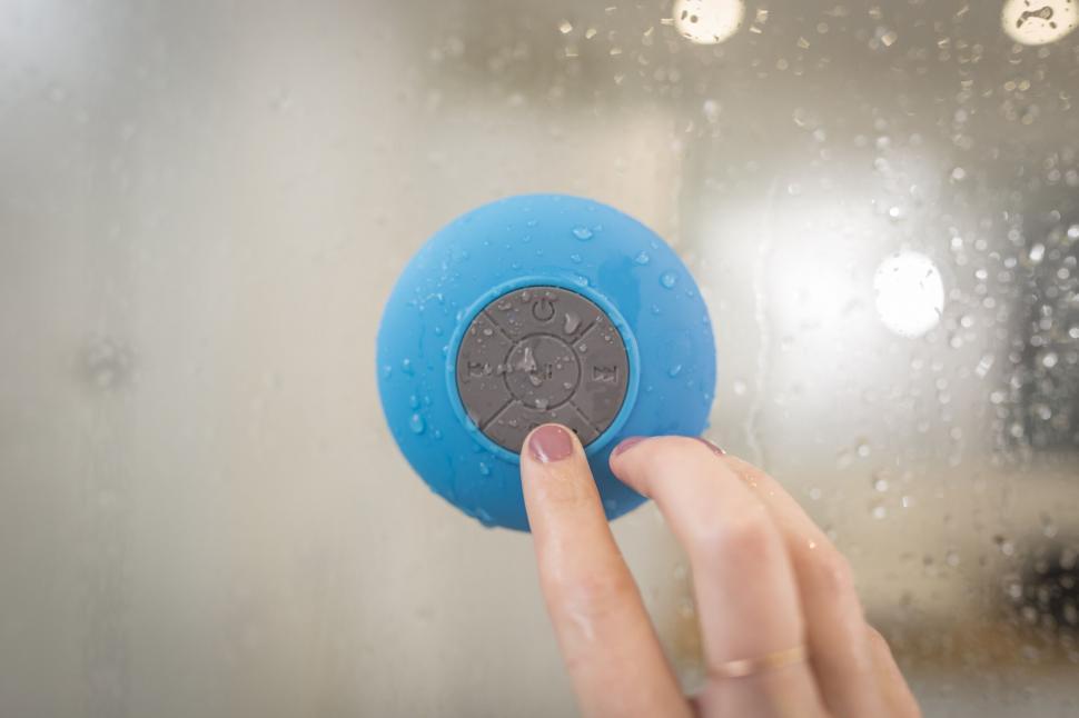 Free Image of Finger pressing a blue Bluetooth speaker button 