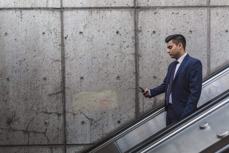 Free Image of Man in suit using phone on escalator 