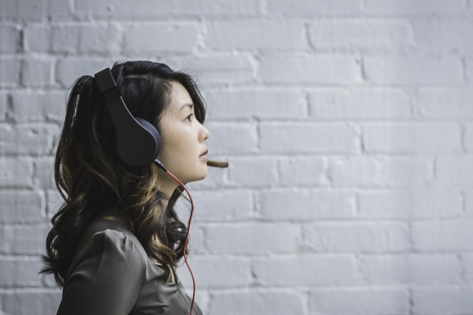 Free Image of Woman with headphones against brick wall 