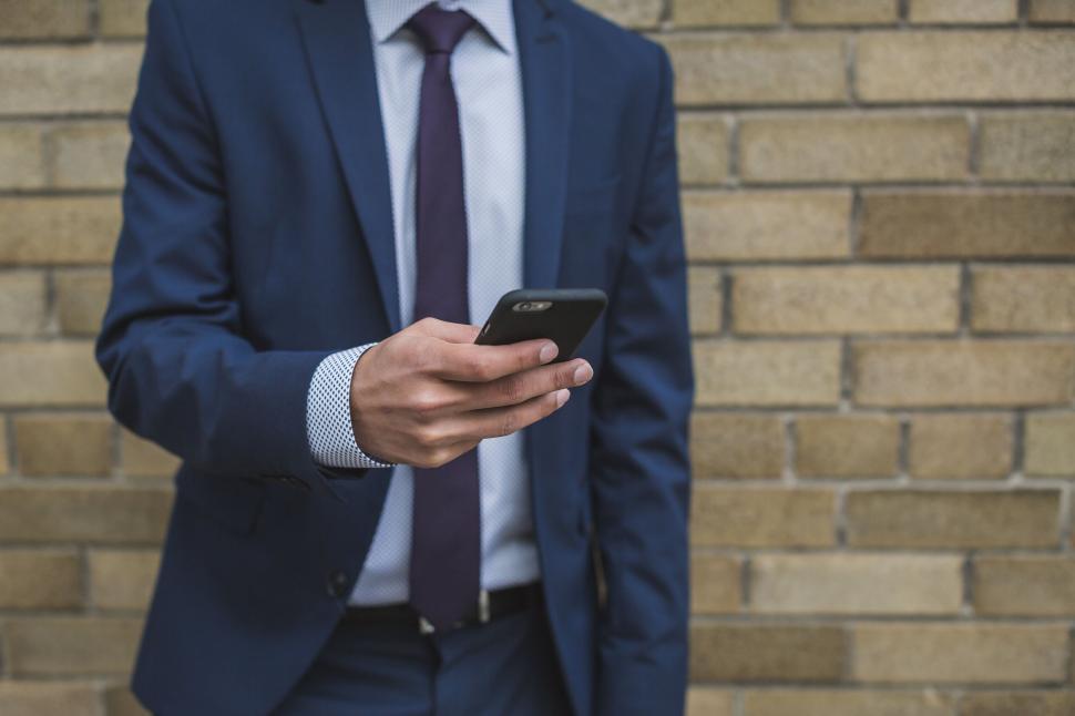 Free Image of Businessman using smartphone by brick wall 
