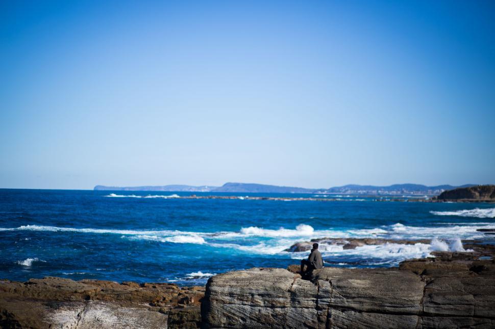 Free Image of Person sitting on the rocky ocean shore 