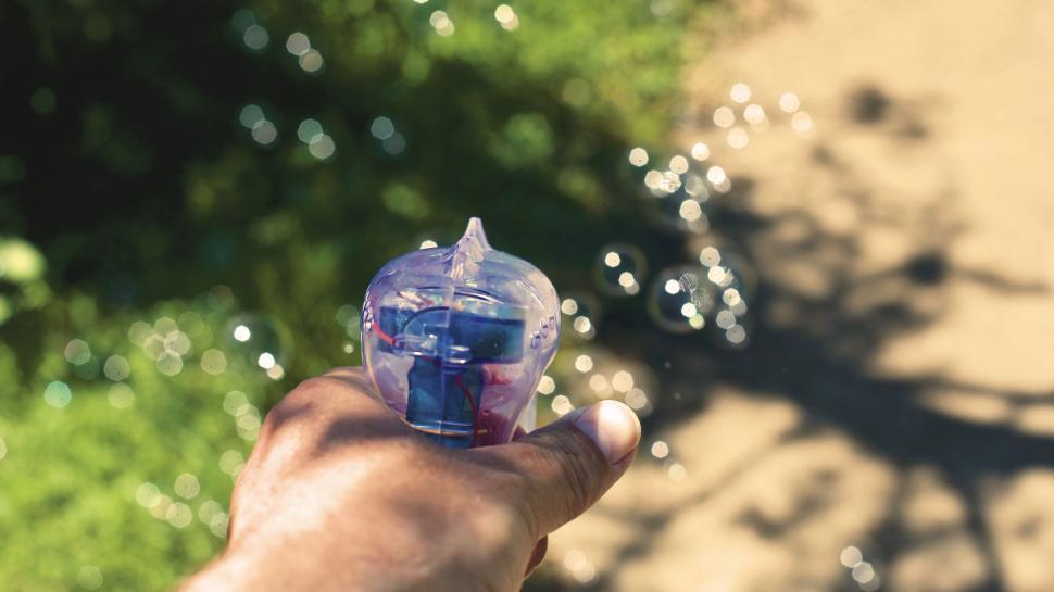 Free Image of Hand holding a bubble blower in sunlight 