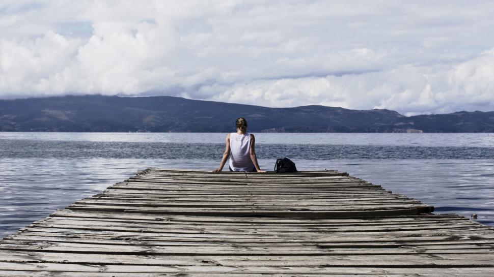 Free Image of Woman sitting on a wooden pier by a lake 