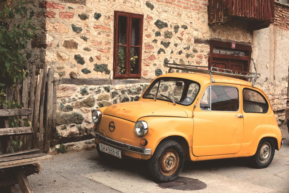 Free Image of Vintage yellow car parked by stone building 