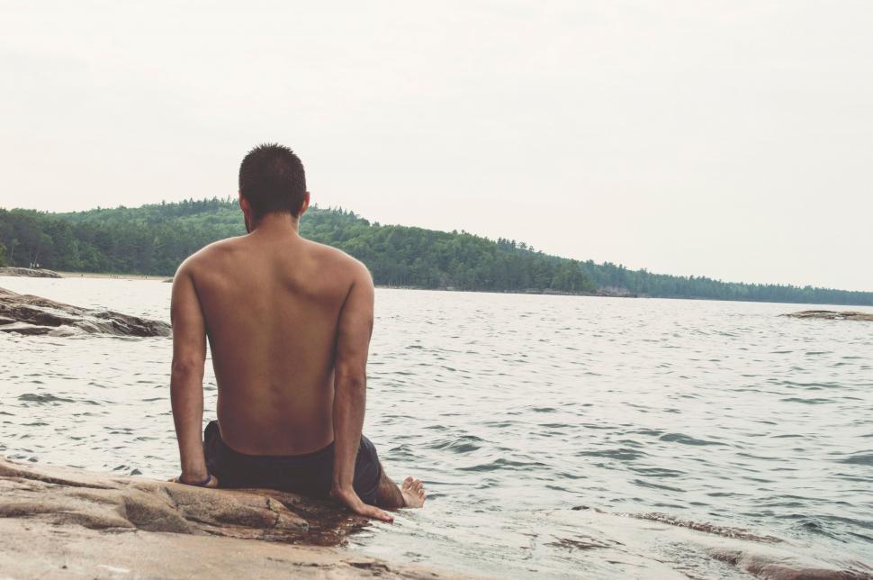 Free Image of Man contemplatively sitting by a lake 
