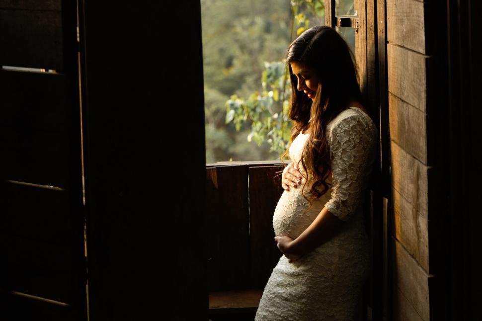 Free Image of Pregnant woman standing by a window 