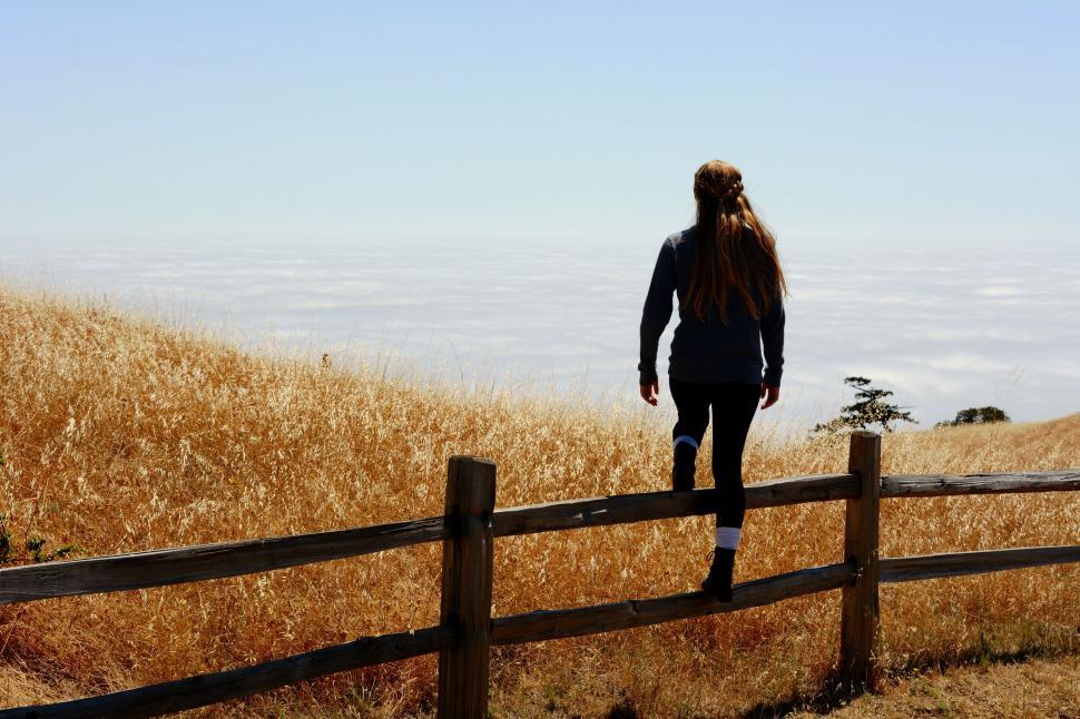 Free Image of Woman walking towards a fence on a hill 