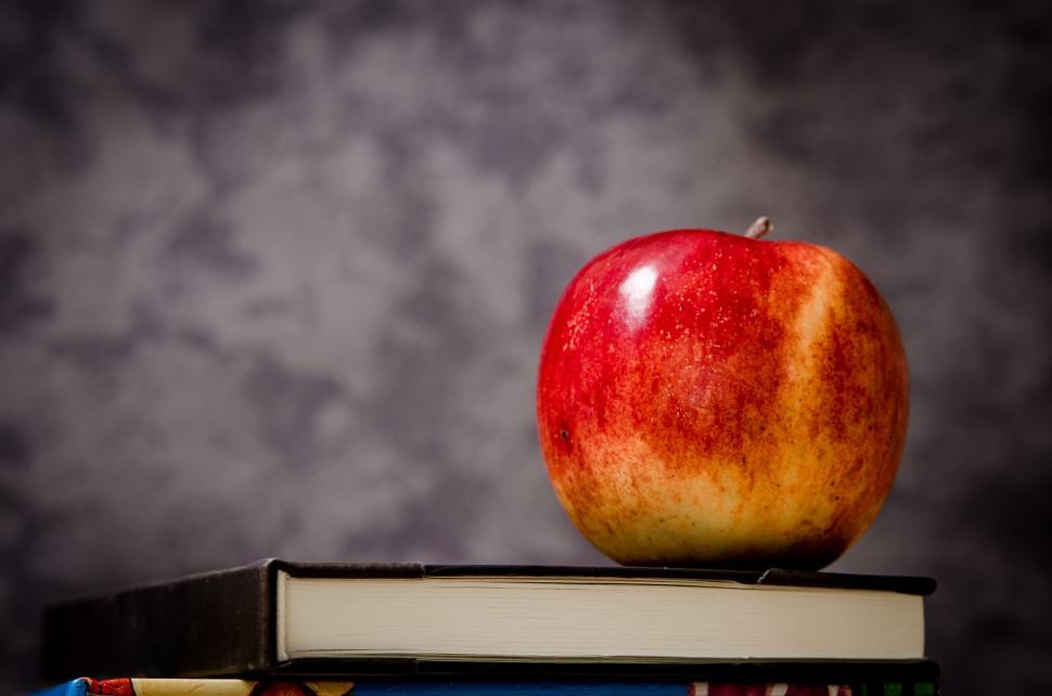 Free Image of Red apple on a pile of books with grey backdrop 