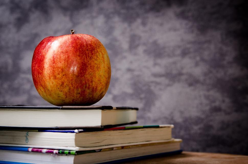 Free Image of Apple on pile of books against grey wall 