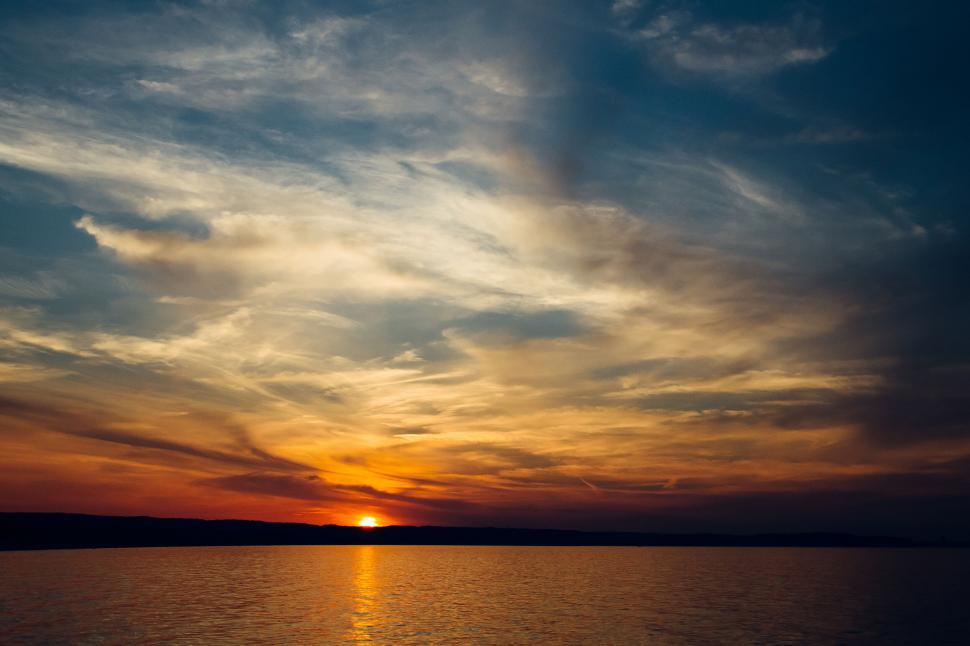 Free Image of Sunset over a tranquil water body with clouds 