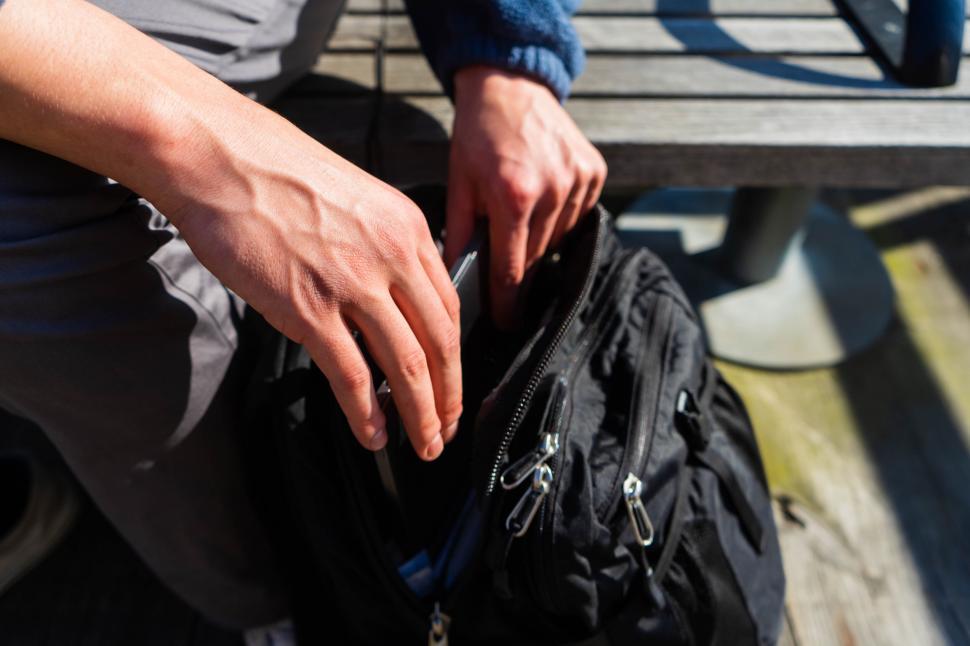 Free Image of Person unzipping black backpack on bench 