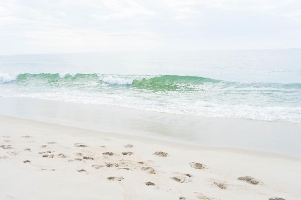 Free Image of Serene beach with waves, footprints, and overcast sky 