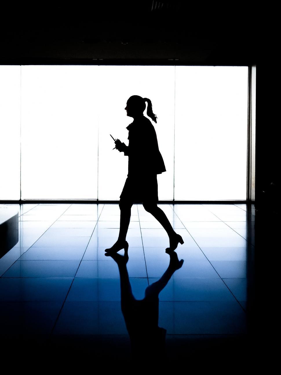 Free Image of Silhouetted woman walking with her mobile phone 