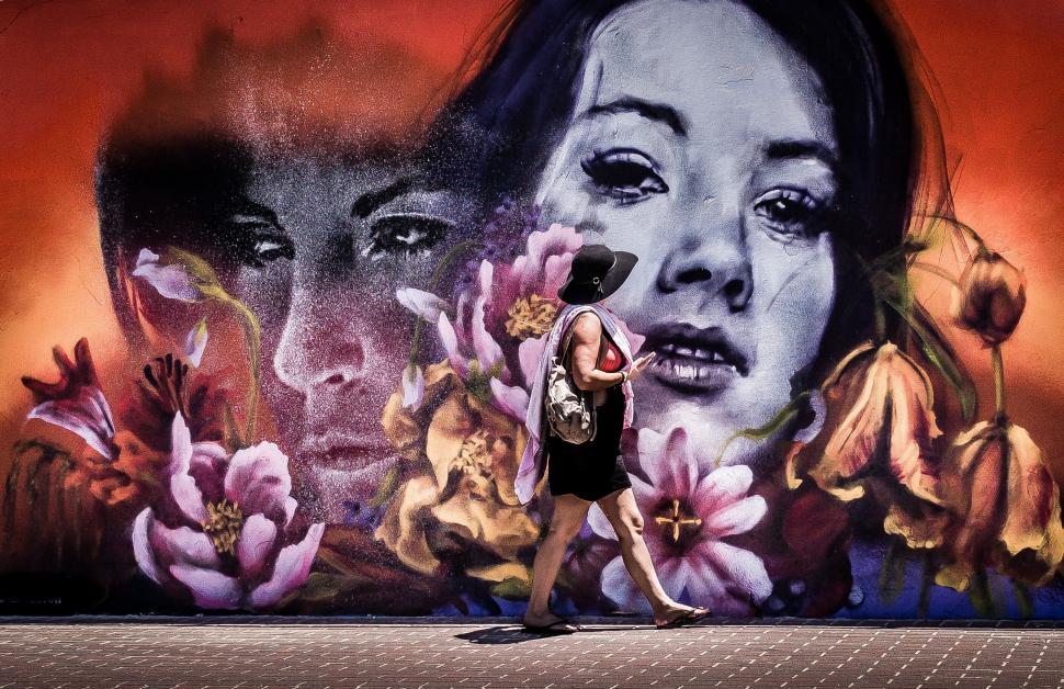 Free Image of Woman walking by a floral graffiti wall 