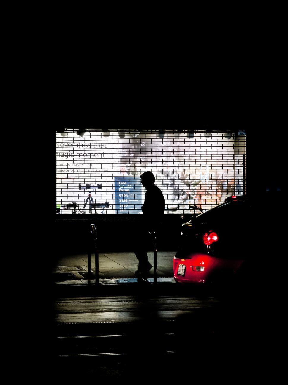 Free Image of Silhouetted figure in car-lit night setting 