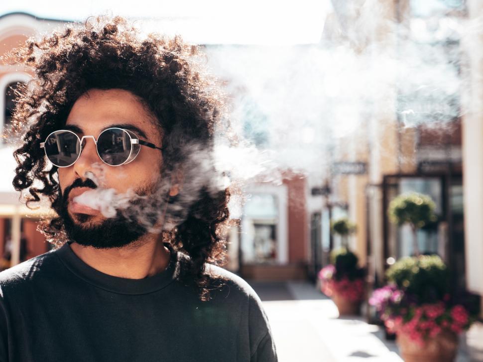 Free Image of A man with curly hair and sunglasses smoking 