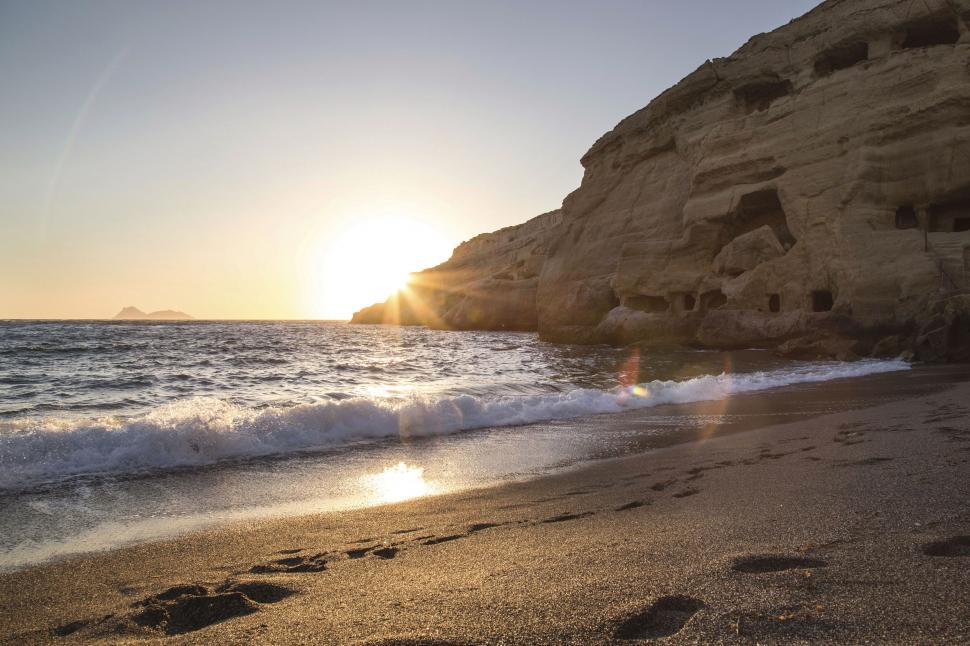 Free Image of Sunset on a serene beach with rock caves 