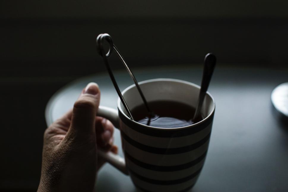 Free Image of Hand stirring hot drink in striped cup in dim light 